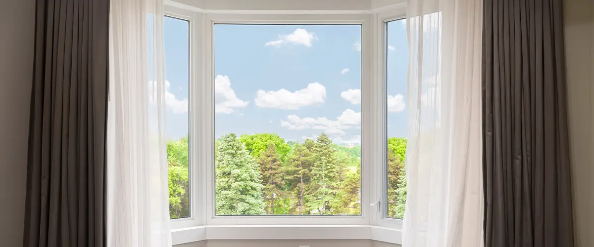 Bright room with bay window, sheer curtains, and forest view for home design.