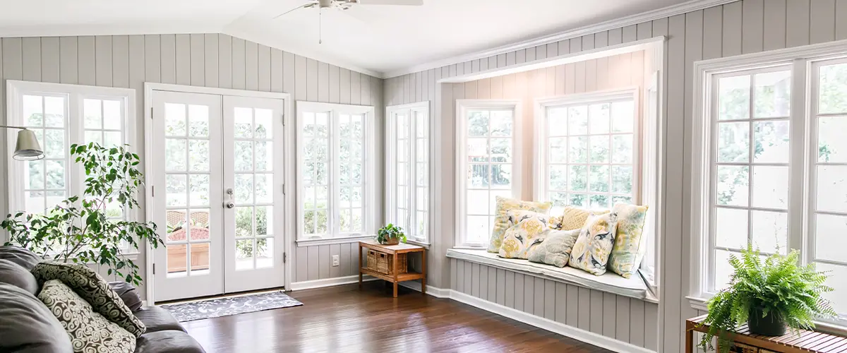 Bright sunroom with hardwood floors, white walls, and cozy seating area.