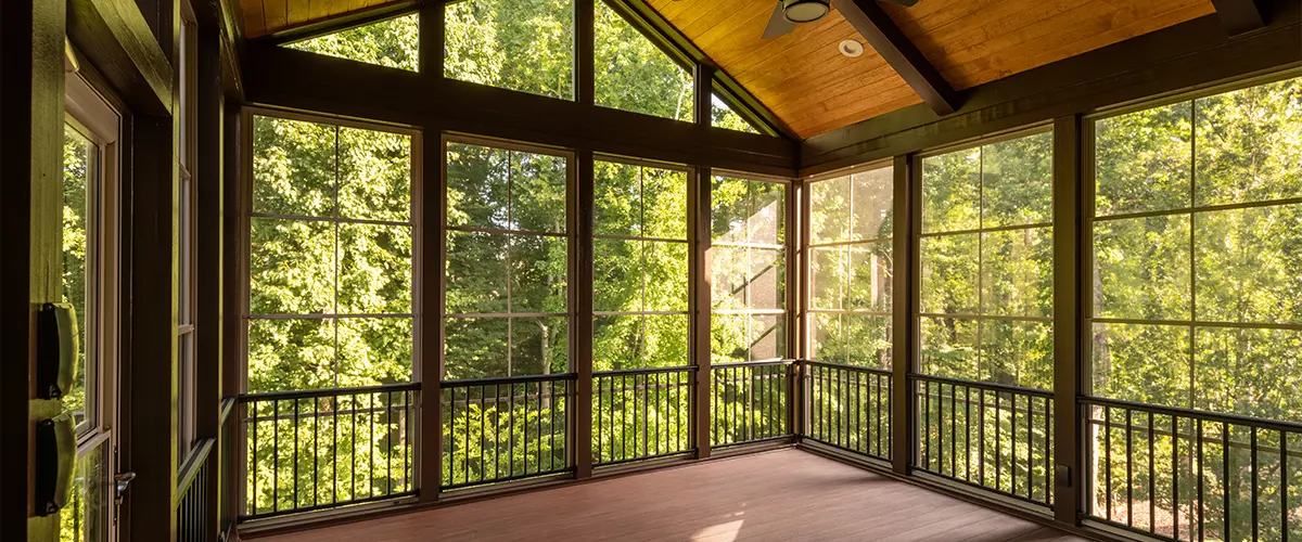 Modern new screened porch with fibrex windows and composite floor with summer woods in the background.