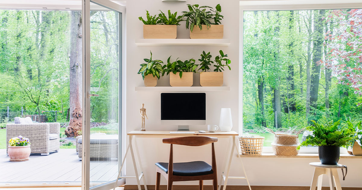 Zen home office with computer in a beautiful, spacious living room interior with plants and an outside view through big windows