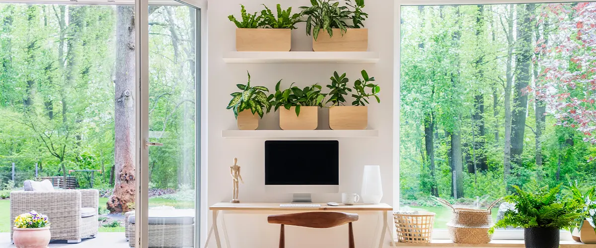 Zen home office with computer in a beautiful, spacious living room interior with plants and an outside view through big windows