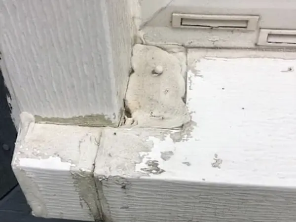 Exterior window frame with significant termite damage, showing peeling paint, wood decay, and termite mud tubes around the corner of the window ledge.