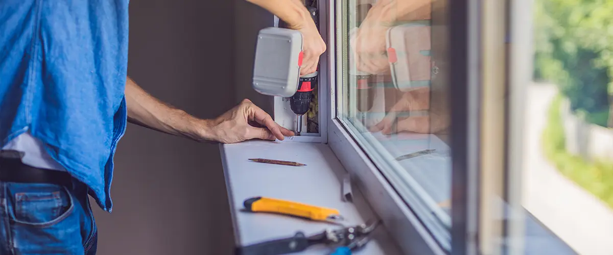 Worker using a power drill window replacement in Franklin, with tools on the sill.