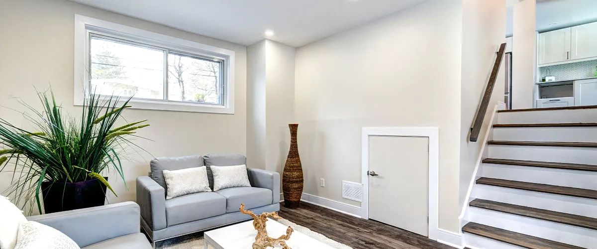 Finished basement with a sliding window above a grey couch, showcasing modern decor with wooden flooring