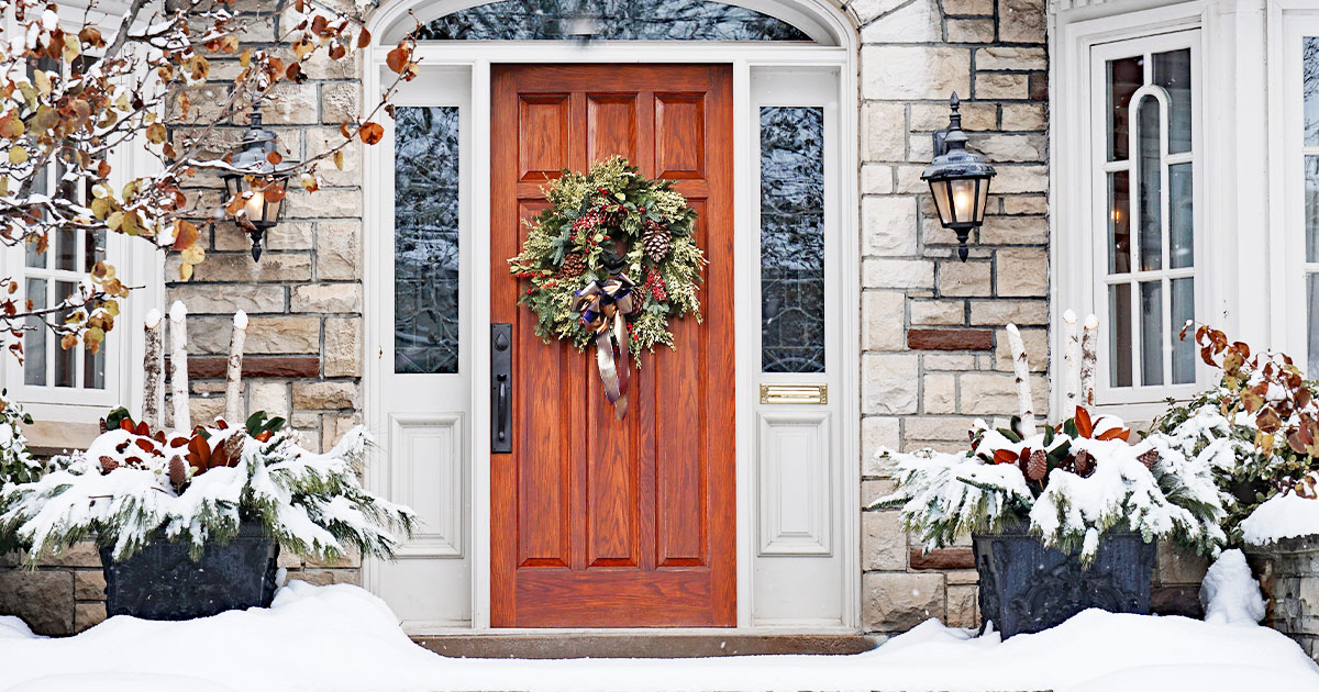 Best exterior doors for cold weather, stone house with a wooden door and Christmas wreath in snowy weather