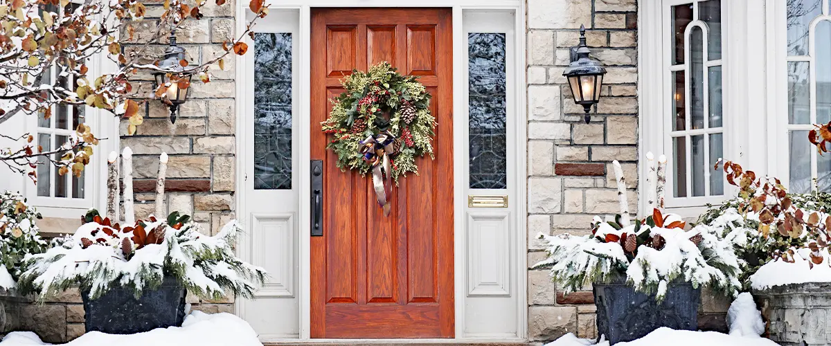 Best exterior doors for cold weather, stone house with a wooden door and Christmas wreath in snowy weather