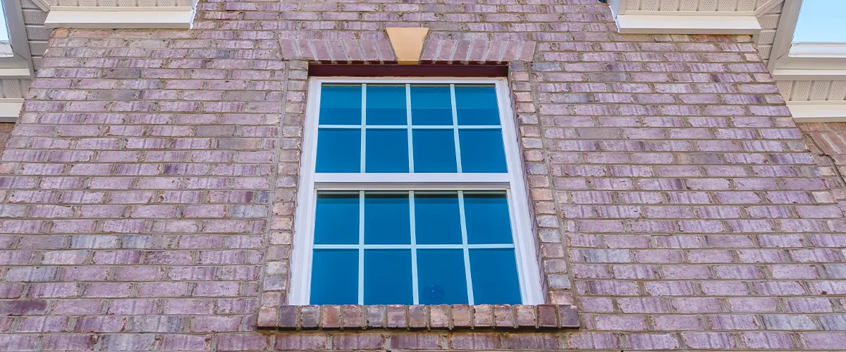 Top floor of a brick house featuring a double-hung window with white trim against a blue sky