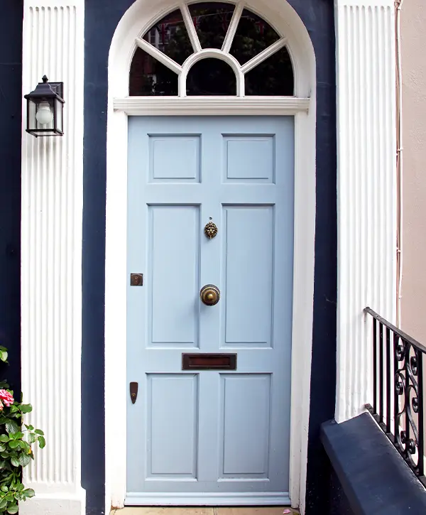 A classic blue front door with an arched transom window, flanked by white columns and a small lantern