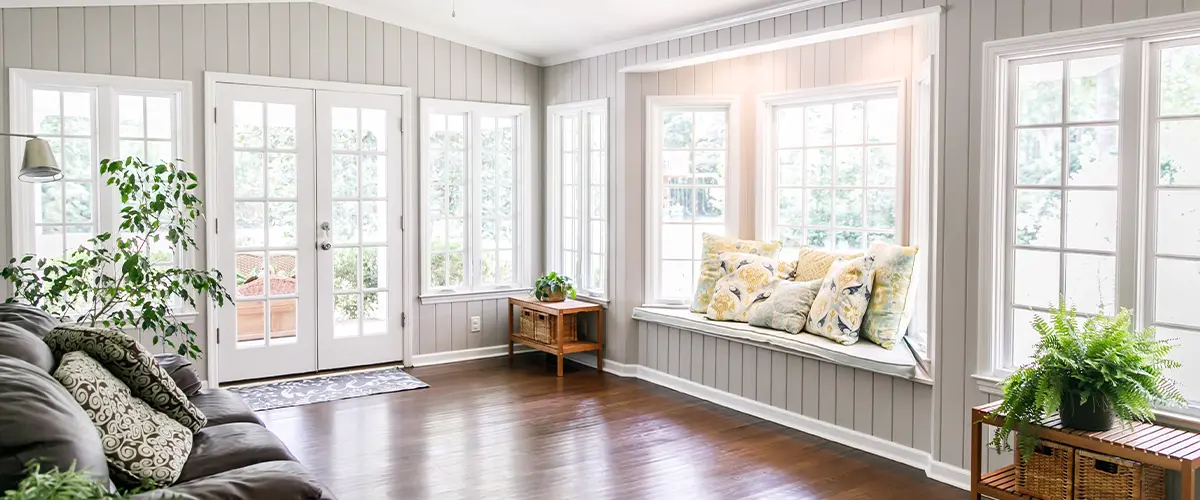 A bright sunroom with large windows, a cozy seating area with cushions, and a hardwood floor