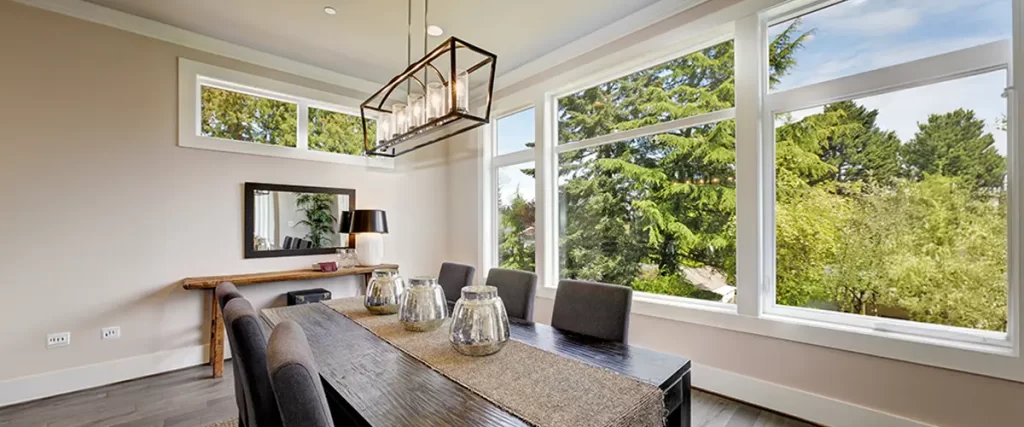 Bright dining room with large picture windows and a modern chandelier. Spacious, natural light-filled home interior.