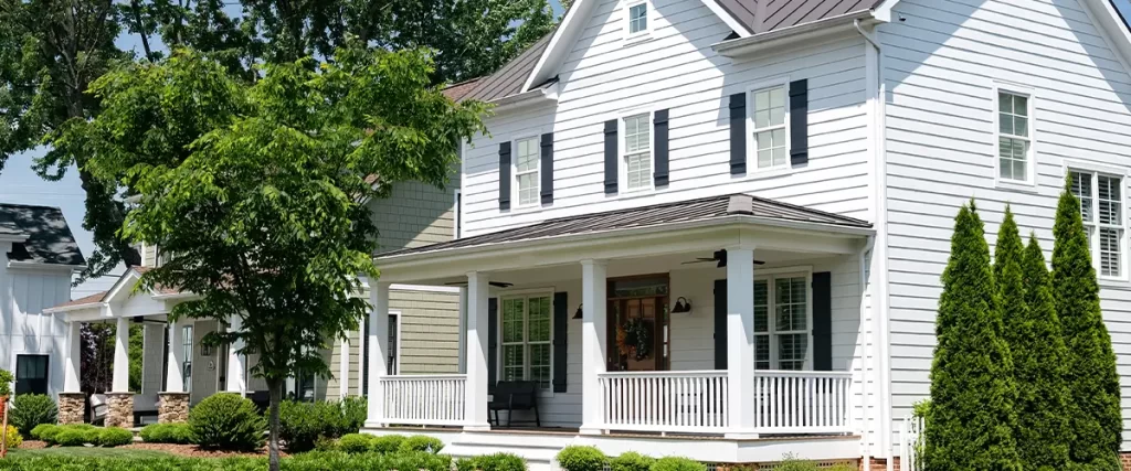 Modern white siding home with black shutters and front porch in a suburban neighborhood with manicured landscaping