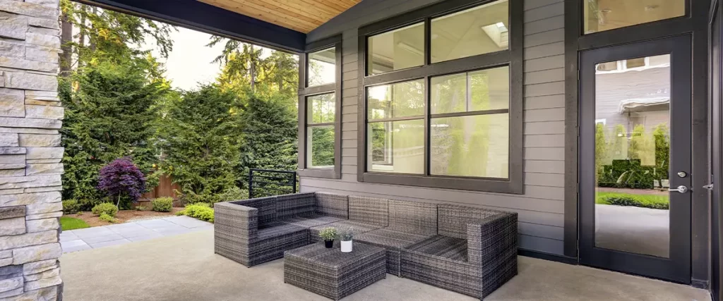 Covered backyard patio with gray siding, wicker furniture, and natural wood ceiling for outdoor living