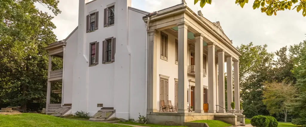 Large historic Southern home with tall white columns and red brick accents surrounded by trees and green lawn