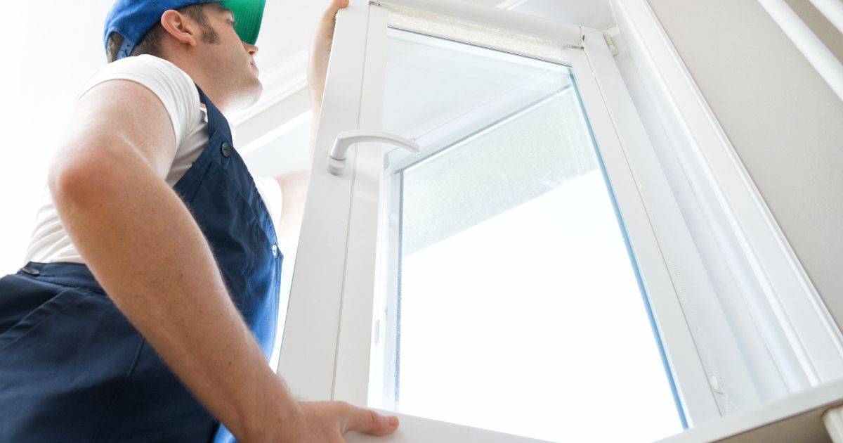 Another angle of a worker positioning a large white-framed window during installation.
