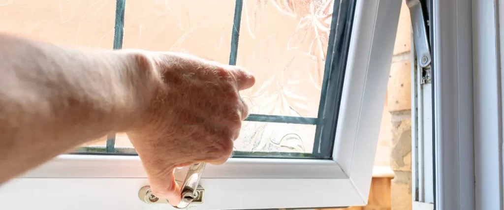 Another close-up of a hand operating a white-framed window latch with frosted glass panels.