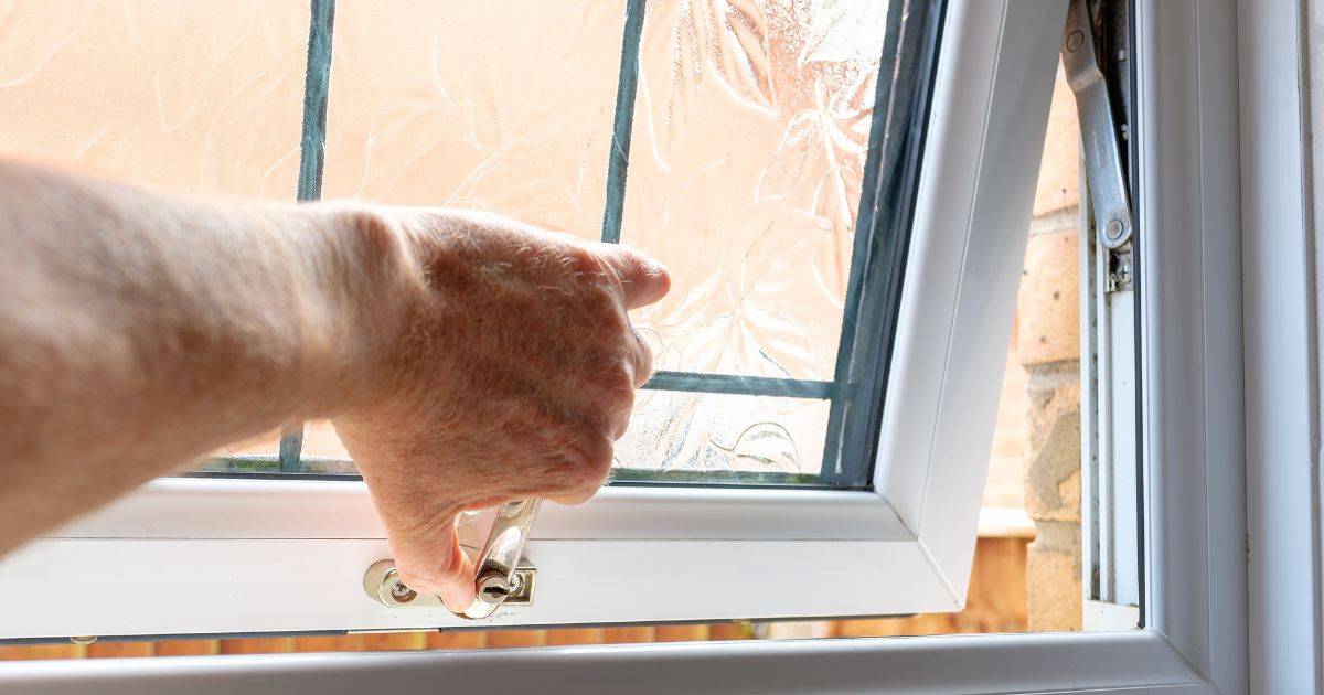Close-up of a hand locking or unlocking a white-framed window with frosted glass.