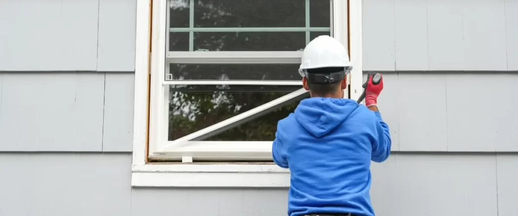A similar view of two workers installing a window frame from outside a house.