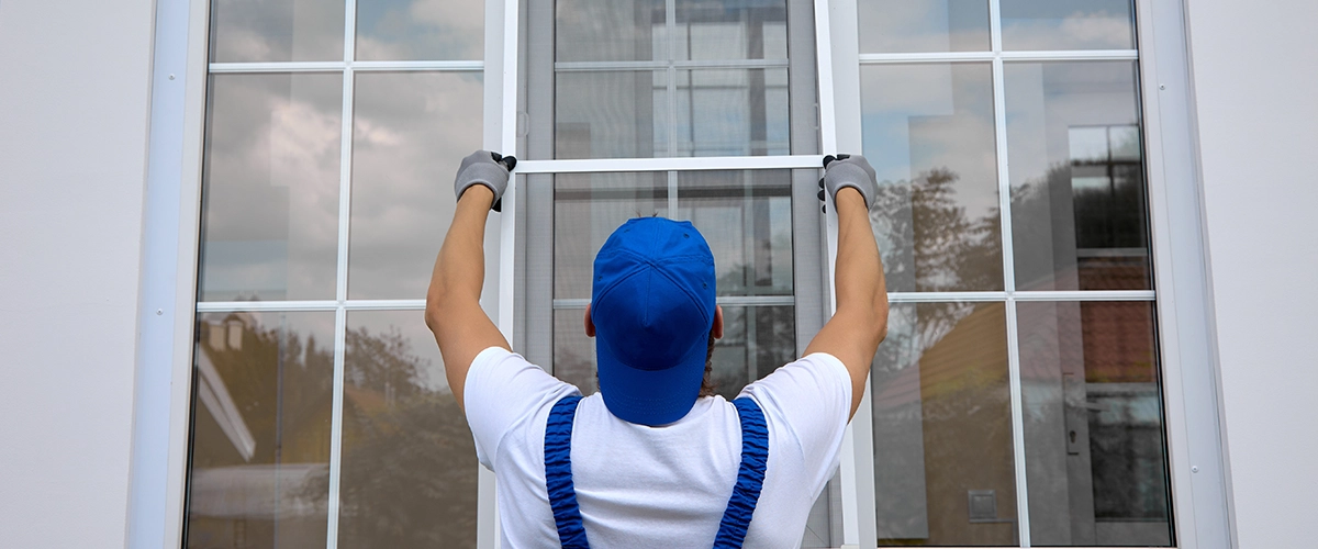 Background of blue-cap worker installing a mosquito net on large plastic window outside the building in summer