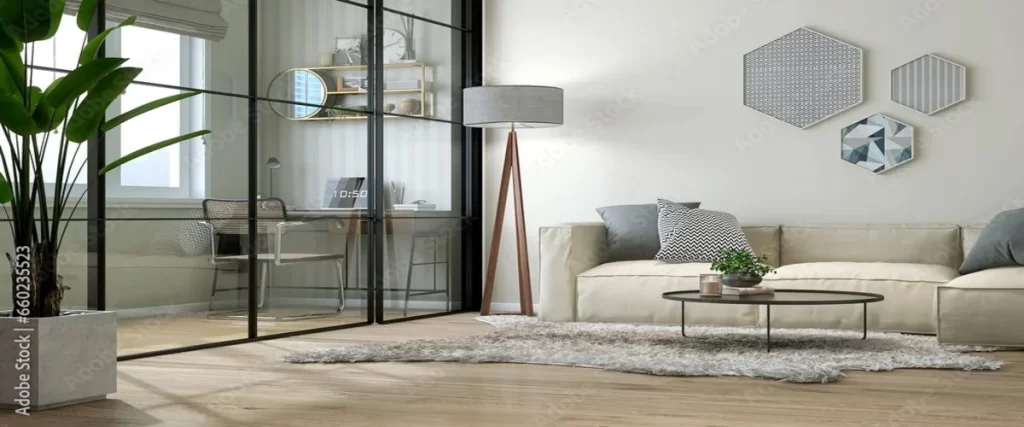A modern living room with a sofa and floor lamp, separated from a home office by a black-framed glass partition wall