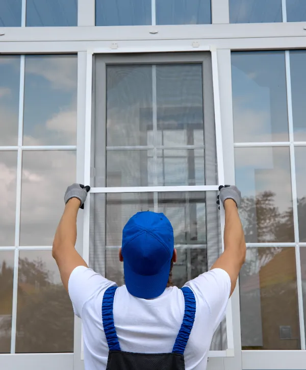 A worker is installing or removing a window screen on a white-framed window