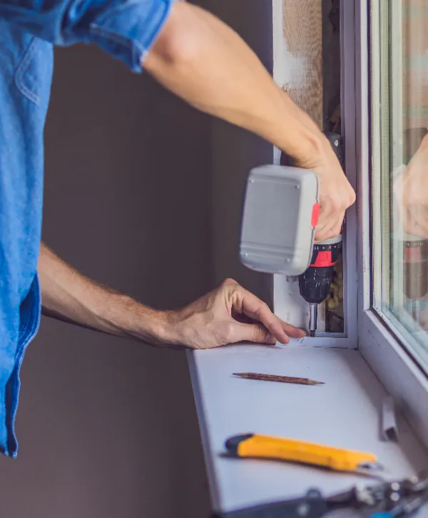 a person installing a window using a power drill.