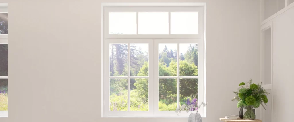 A large, clean white multi-pane window in a minimalist room offering a clear view of a lush green forest and garden.