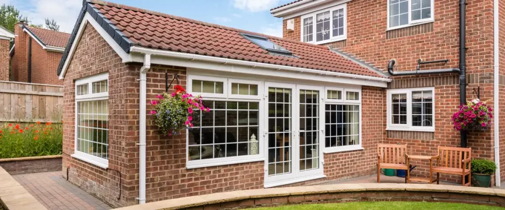 Exterior view of a traditional brick home featuring a sunroom extension with bright white gridded windows and matching french doors.