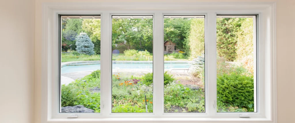 Interior view of a large four-pane white window providing superior noise reduction while overlooking a lush backyard, swimming pool, and garden landscape.