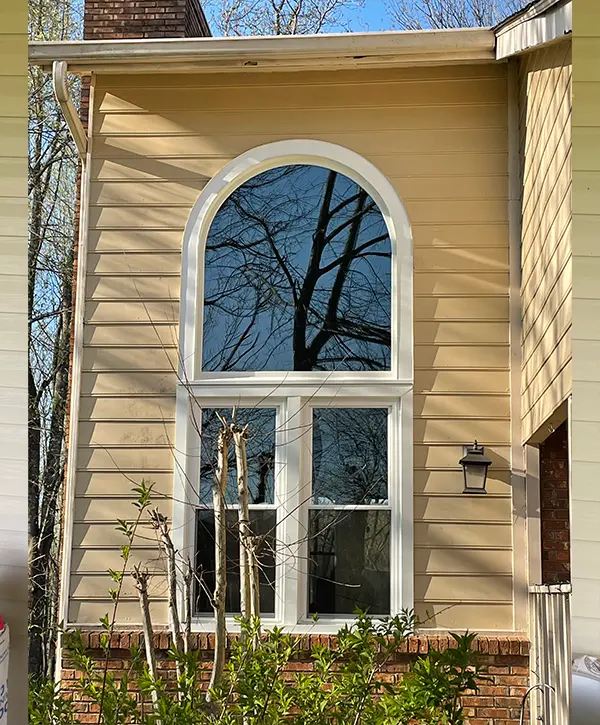 Arched replacement window installation on two-story home exterior with vinyl siding